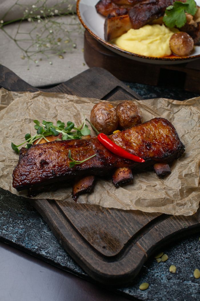 Rustic presentation of grilled rib roast with potatoes and greens, served on a wooden board.